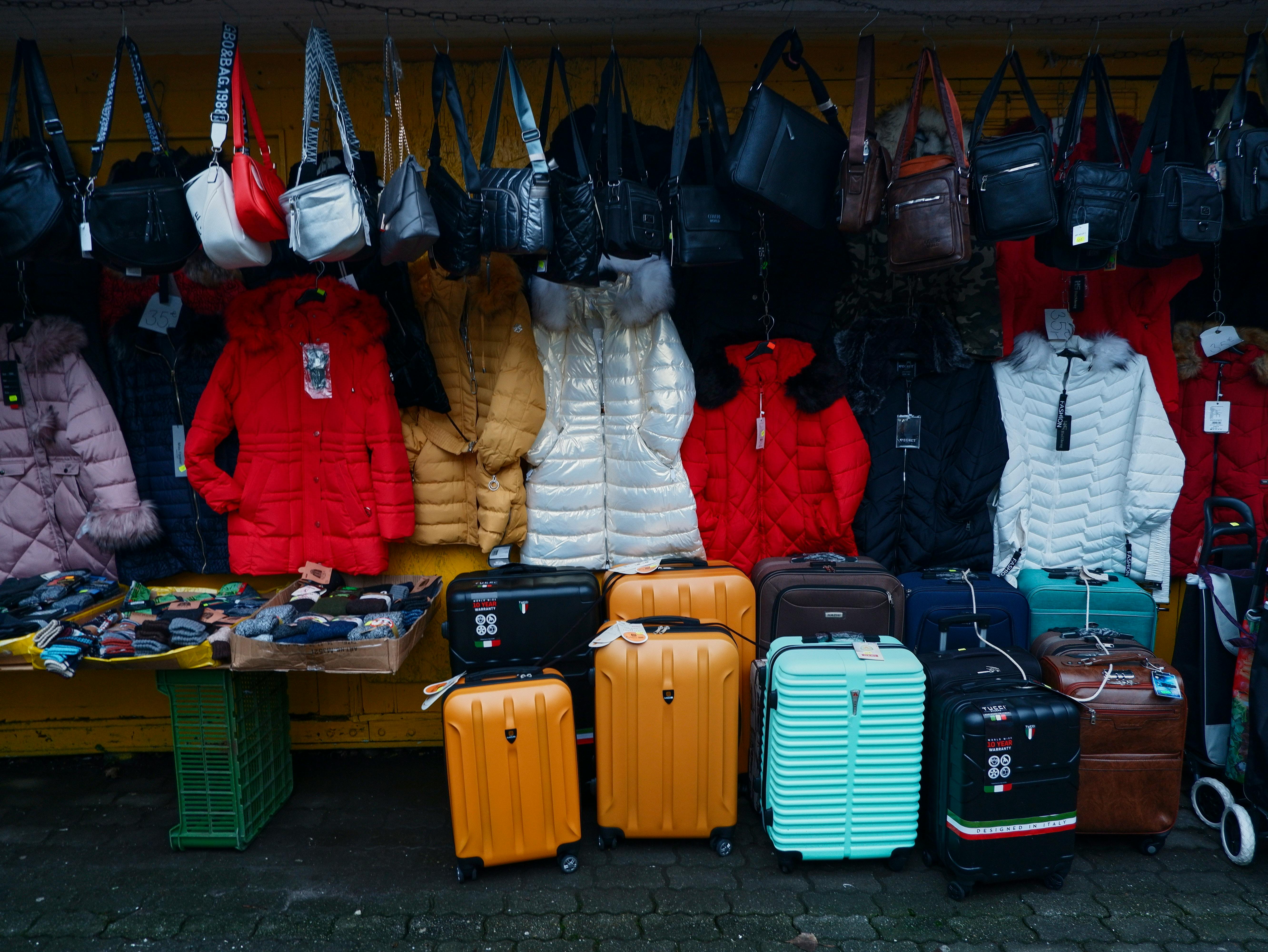 A street stall with luggage, purses, and coats.